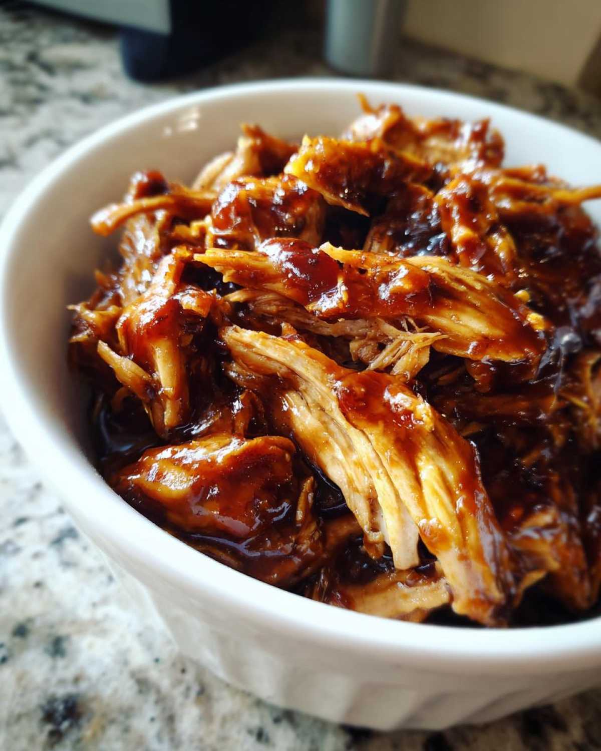 Close-up of shredded crockpot teriyaki chicken coated in a thick, glossy teriyaki sauce, served in a white bowl.