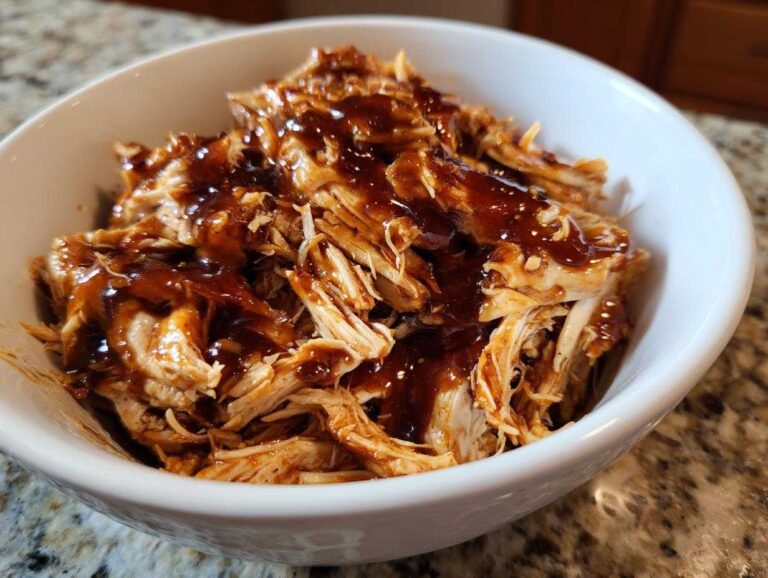 Close-up of shredded crockpot teriyaki chicken generously drizzled with thick teriyaki sauce in a white bowl.