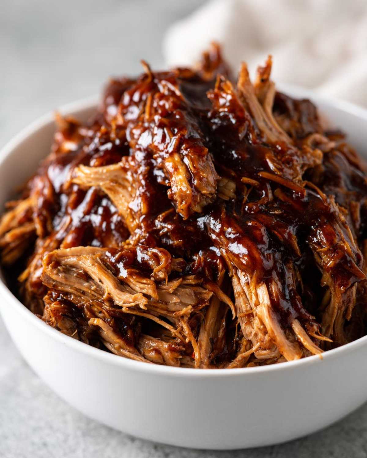 Close-up of shredded crockpot teriyaki chicken heavily coated in a thick, glossy teriyaki sauce in a white bowl.