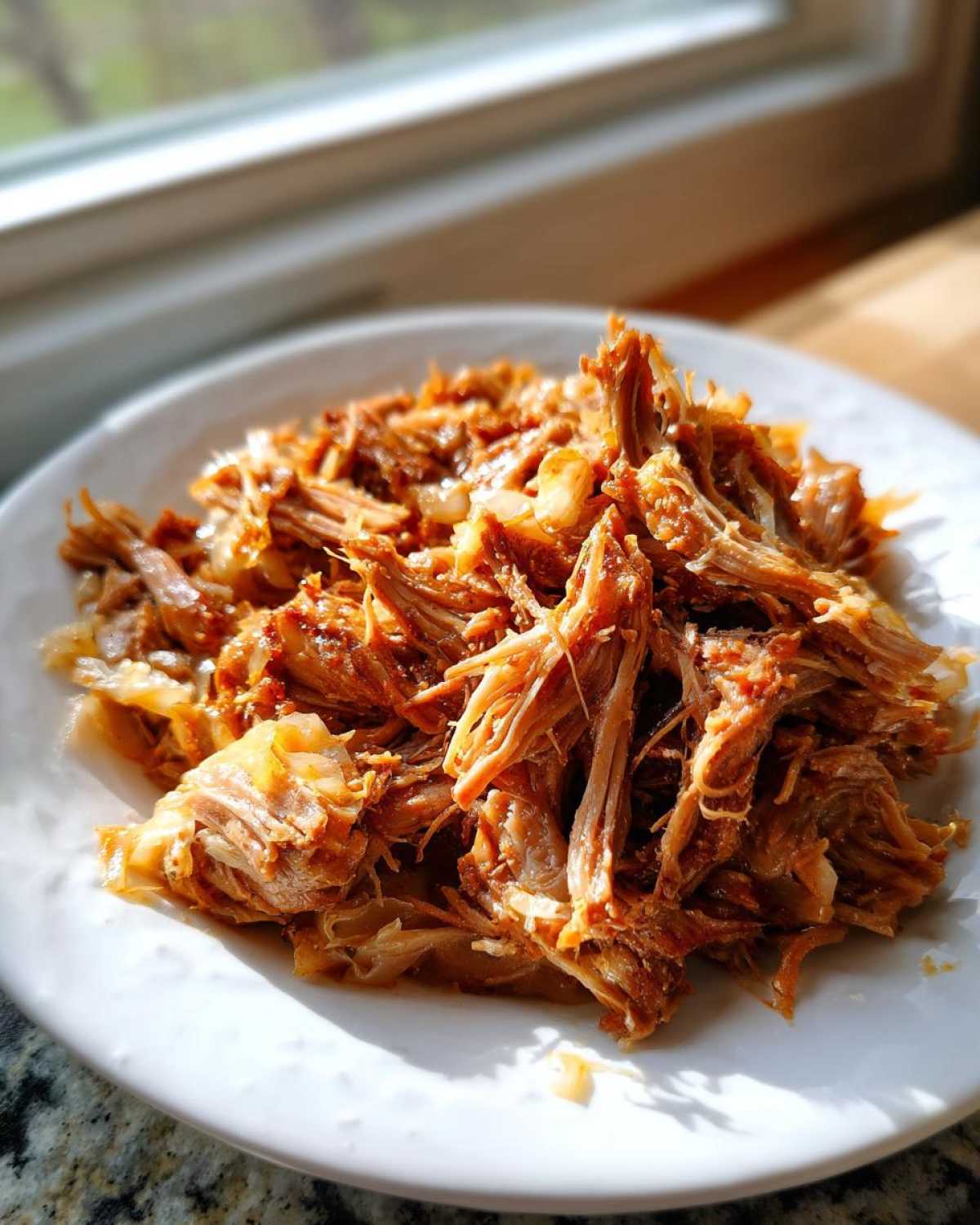 A close-up of tender, shredded pork and sauerkraut mixture served on a white plate.
