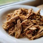 Close-up of tender, shredded pork and sauerkraut mixture served in a white bowl.