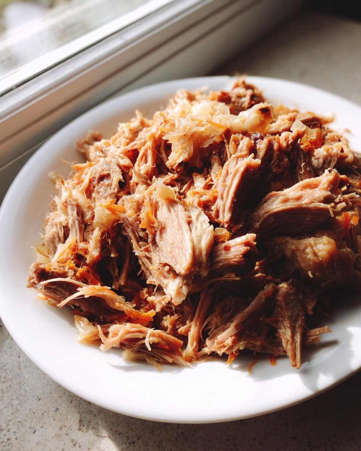 A mound of shredded pork and sauerkraut mixture served on a white plate, brightly lit by natural light.