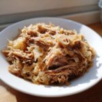 Close-up of shredded pork and sauerkraut mixture served on a white plate, highlighting the texture of the pork and sauerkraut.