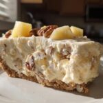 A close-up slice of creamy million dollar pie featuring pineapple chunks and pecans in a graham cracker crust.