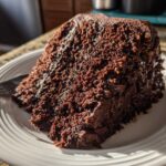 A generous slice of moist german chocolate cake recipe covered in dark, textured frosting on a white plate.
