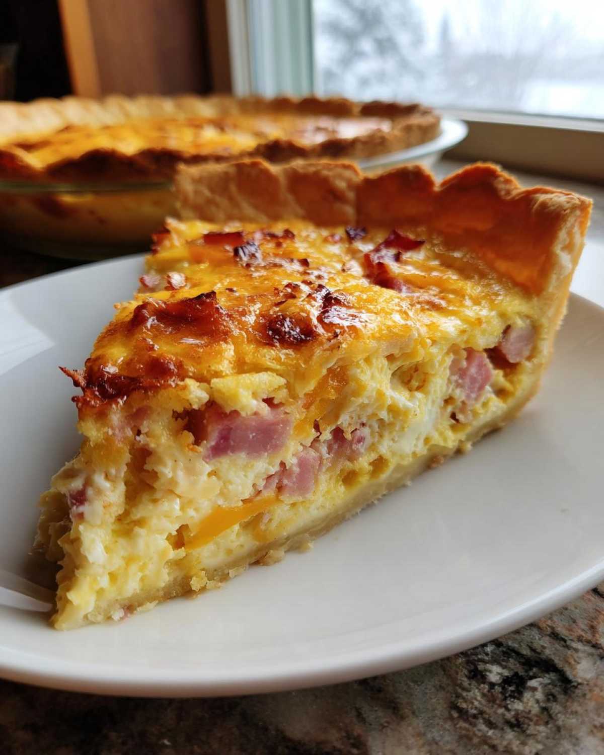A thick slice of golden-brown Ham and Cheese Quiche with visible chunks of ham and melted cheese filling.