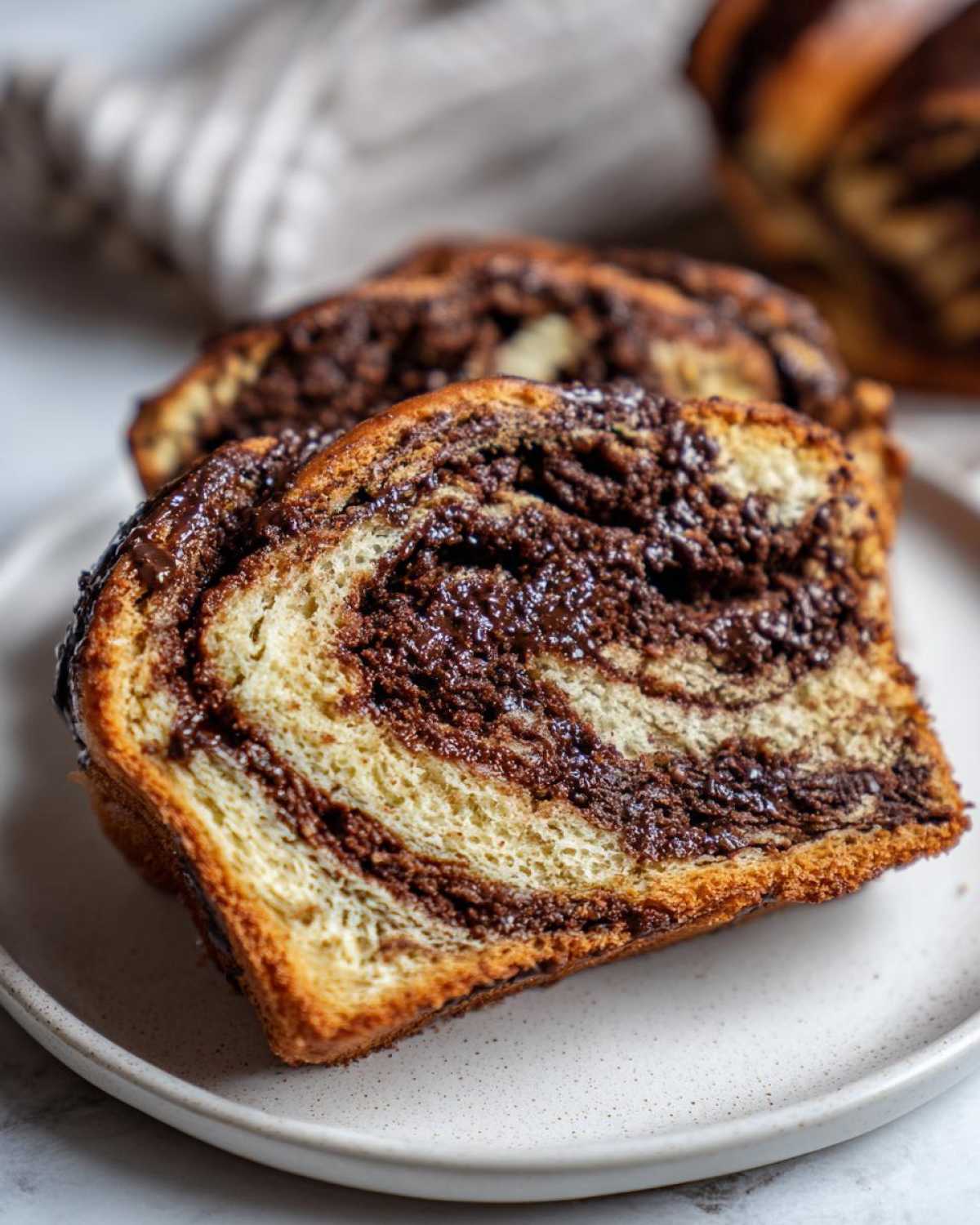 Close-up of two thick slices of moist chocolate babka showing the beautiful swirl of dark chocolate filling and light dough.