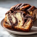 A thick slice of moist chocolate babka showing rich chocolate swirls next to the rest of the loaf.