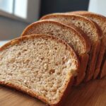 Close-up of several slices of homemade whole wheat bread fanned out on a wooden cutting board.