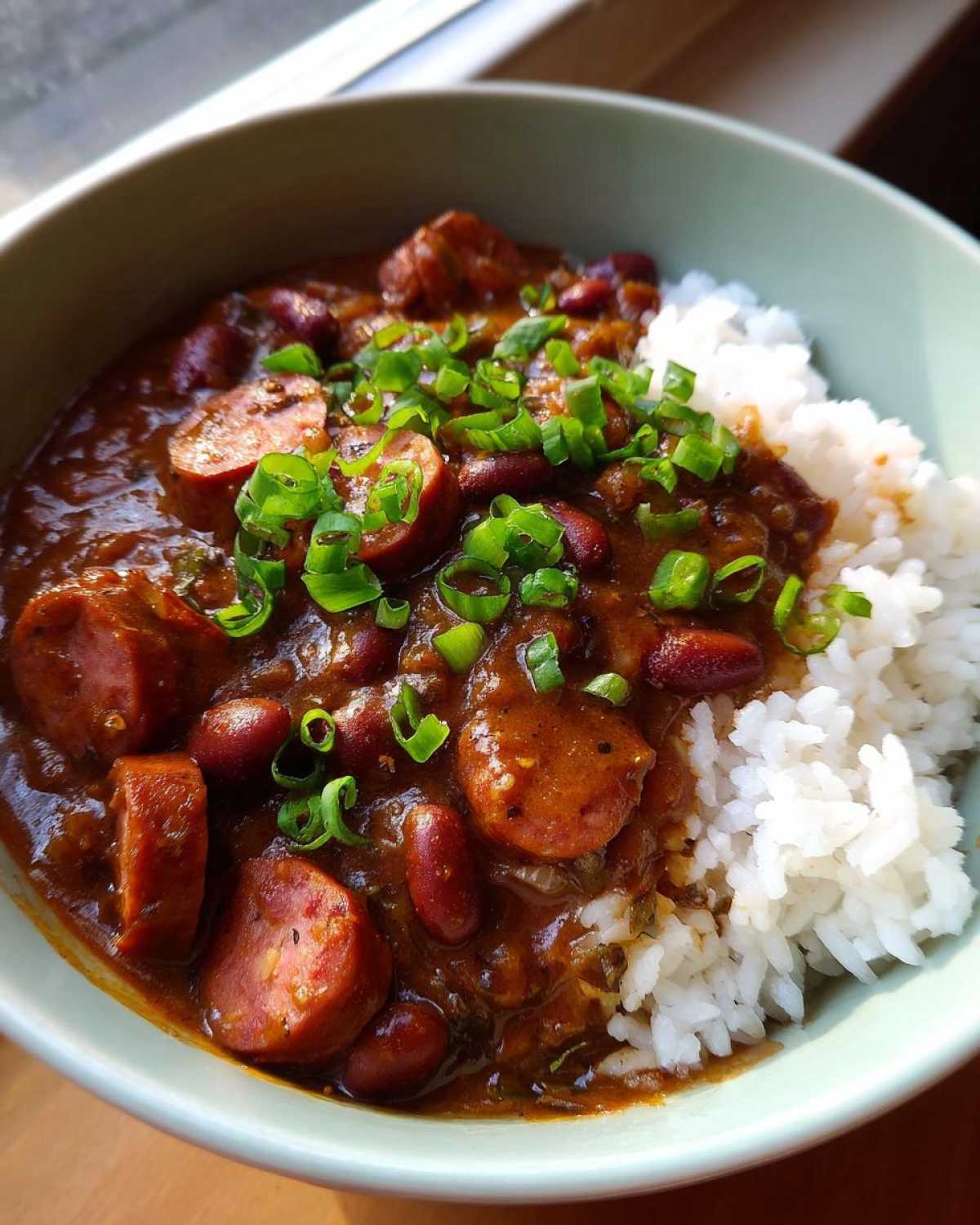 A close-up of a bowl of rich slow cooker red beans and rice topped with sliced sausage and green onions.