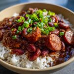A close-up of slow cooker red beans and rice topped with sliced andouille sausage and green onions.