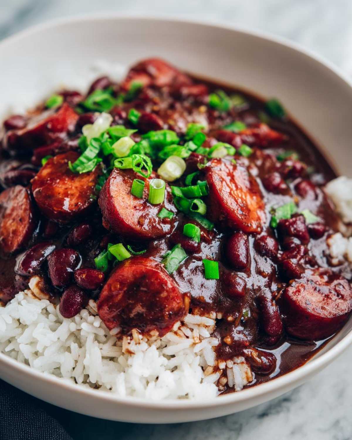 Close-up of a bowl of rich slow cooker red beans and rice topped with sliced sausage and green onions.