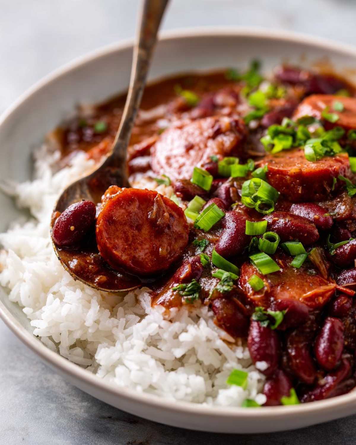 Close-up of a spoonful of rich slow cooker red beans and rice topped with sliced sausage and green onions.