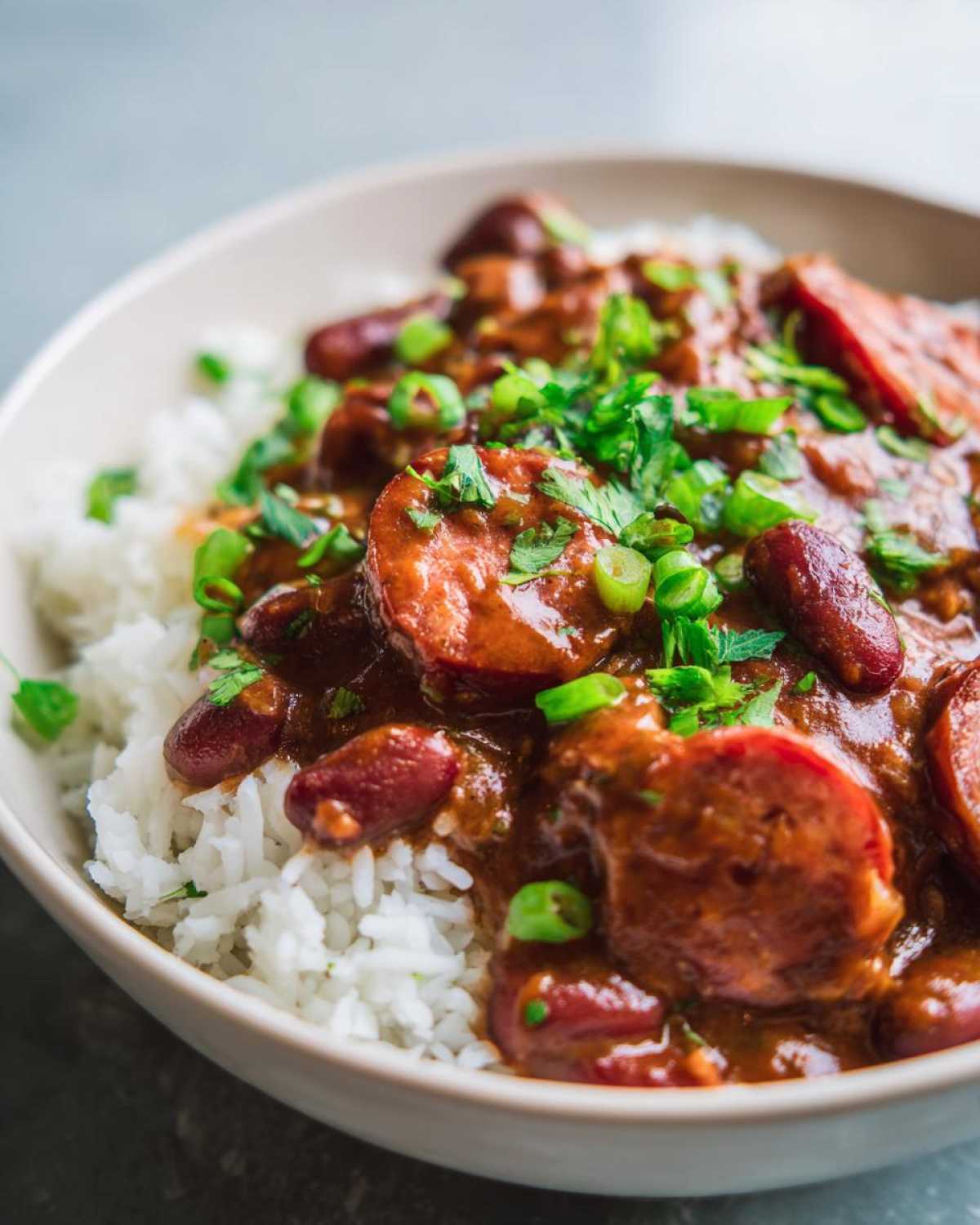 Close-up of a bowl of slow cooker red beans and rice topped with sliced sausage and green onions.