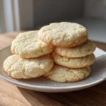 A stack of six freshly baked soft sugar cookies, lightly coated in granulated sugar, resting on a light gray plate.