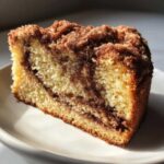 Close-up of a moist slice of sour cream coffee cake featuring a cinnamon swirl and crumbly streusel topping.