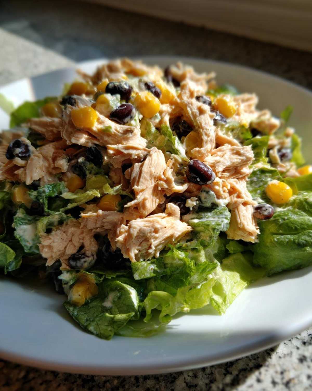 A close-up serving of creamy southwest chicken salad piled high on crisp lettuce, featuring shredded chicken, black beans, and corn.