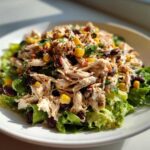 A close-up shot of a vibrant Southwest chicken salad featuring shredded chicken, black beans, and corn over lettuce.