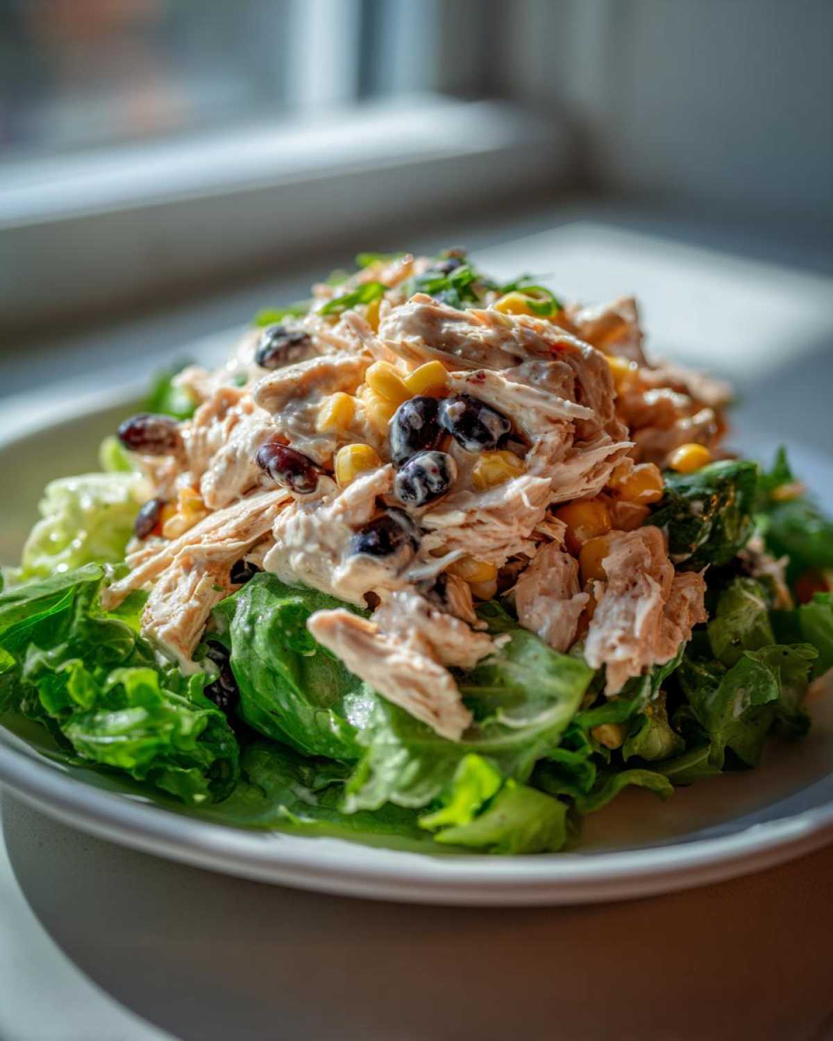 A mound of creamy southwest chicken salad featuring shredded chicken, corn, and black beans served over crisp green lettuce.