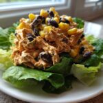 A mound of creamy southwest chicken salad mixed with black beans and corn, served on crisp green lettuce leaves.