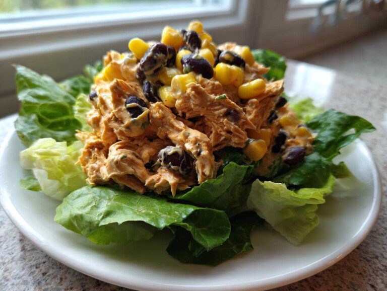 A mound of creamy southwest chicken salad mixed with black beans and corn, served on crisp green lettuce leaves.