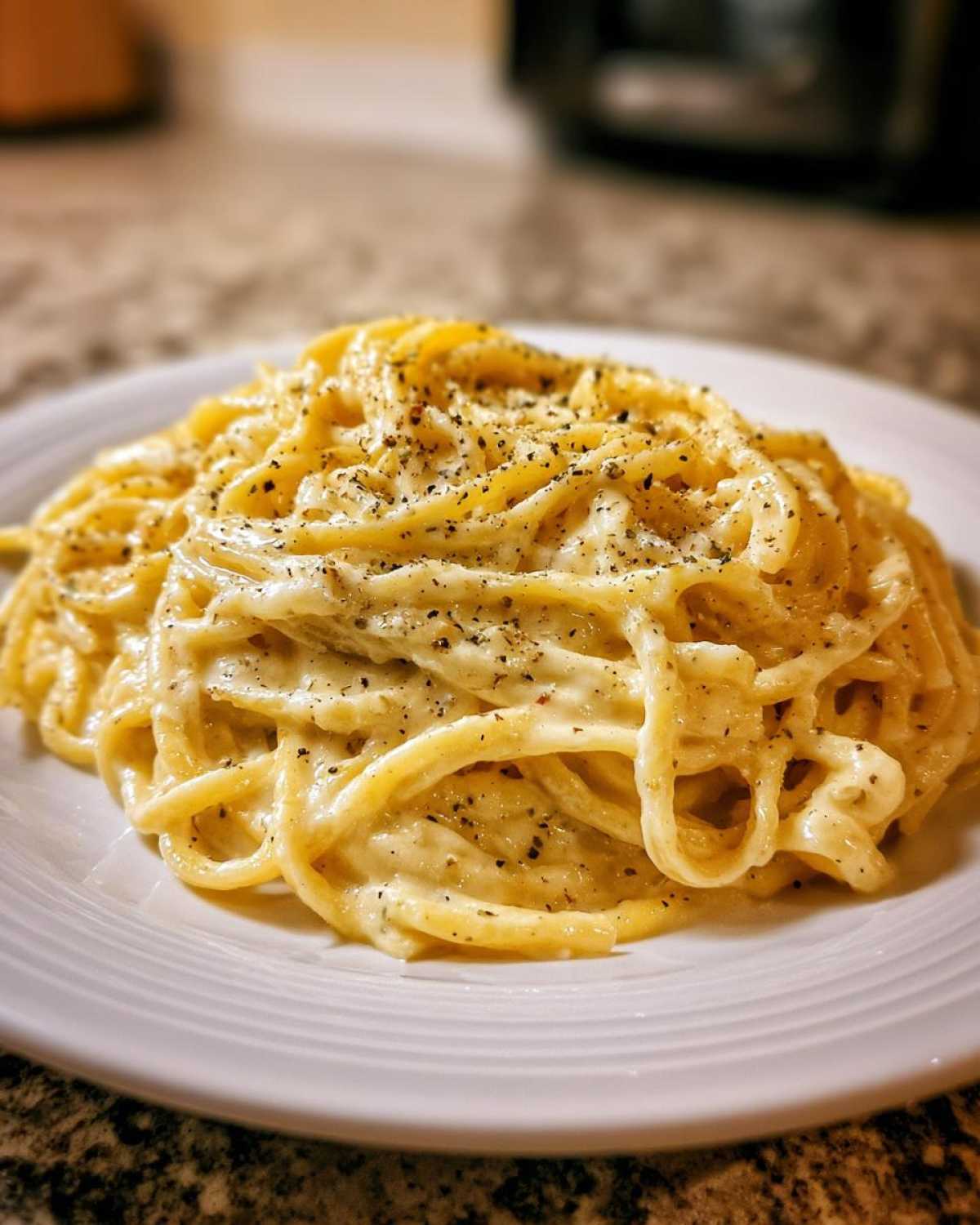 A close-up of spaghetti noodles coated in creamy Olive Garden Alfredo sauce and topped with fresh black pepper.