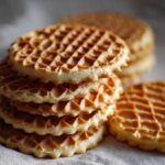 Close-up of a stack of light golden pizzelle cookies showing their distinct waffle pattern texture.