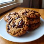 A close-up of a stack of freshly baked vegan chocolate chip cookies with melted chocolate chunks on a white plate.