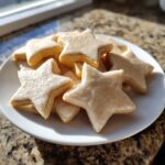 A pile of star-shaped vegan sugar cookies topped with a thin white glaze and sprinkled with cinnamon sugar.