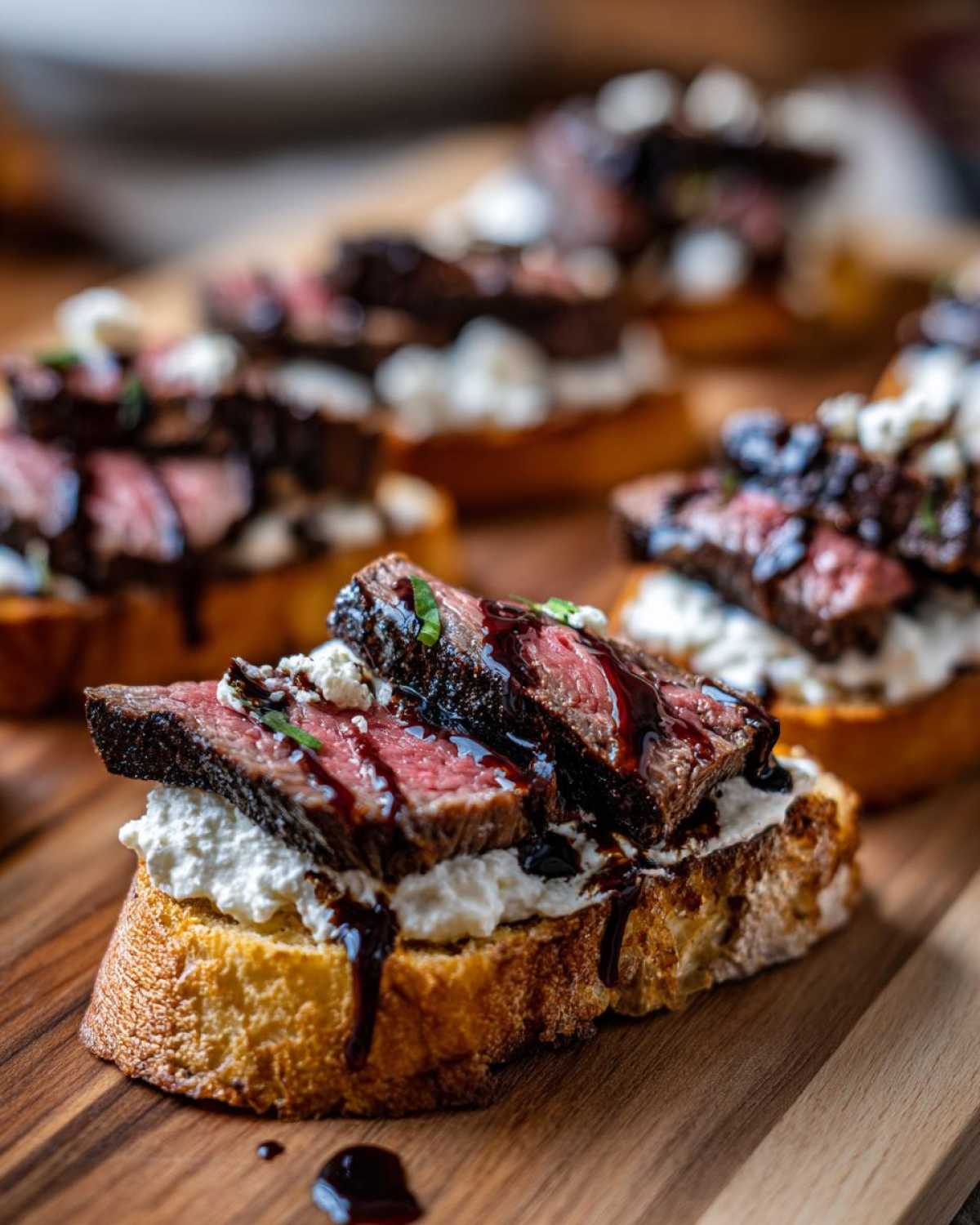 Close-up of a single steak crostini topped with creamy cheese and drizzled with balsamic glaze.