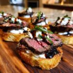 Close-up of a perfectly cooked steak crostini topped with creamy cheese, balsamic glaze, and fresh herbs.