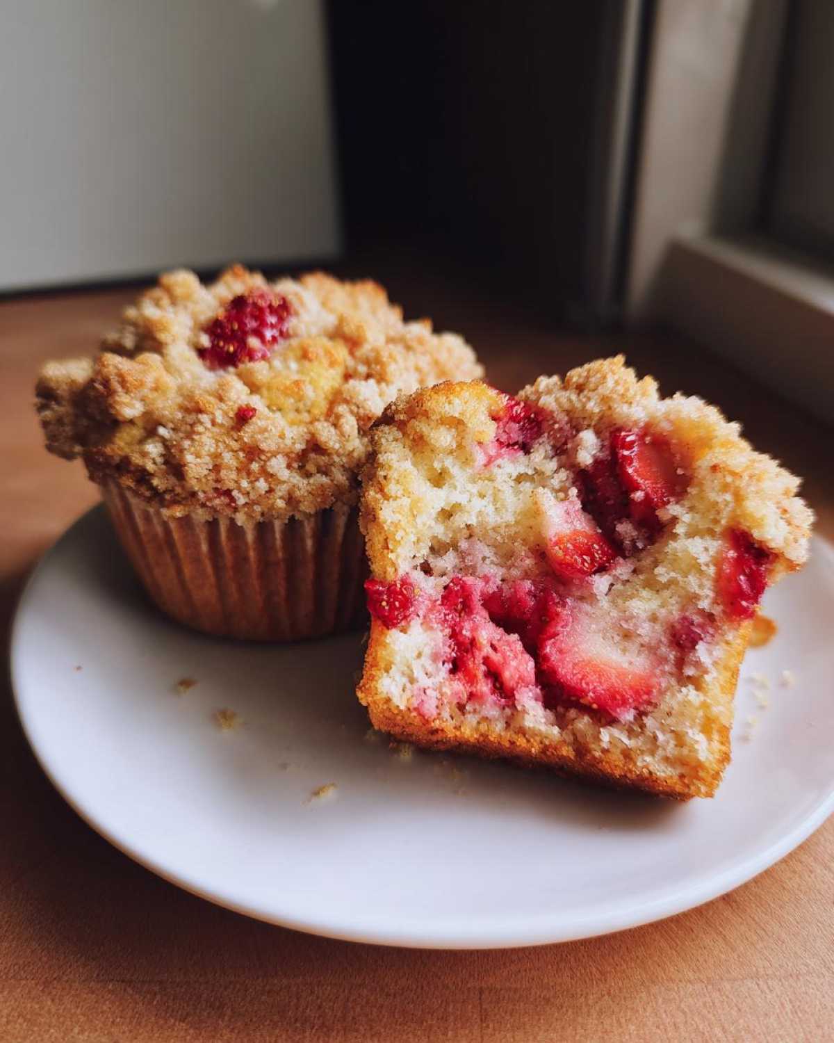 Close-up of two strawberry muffins, one whole and one halved to show the moist interior filled with strawberries.