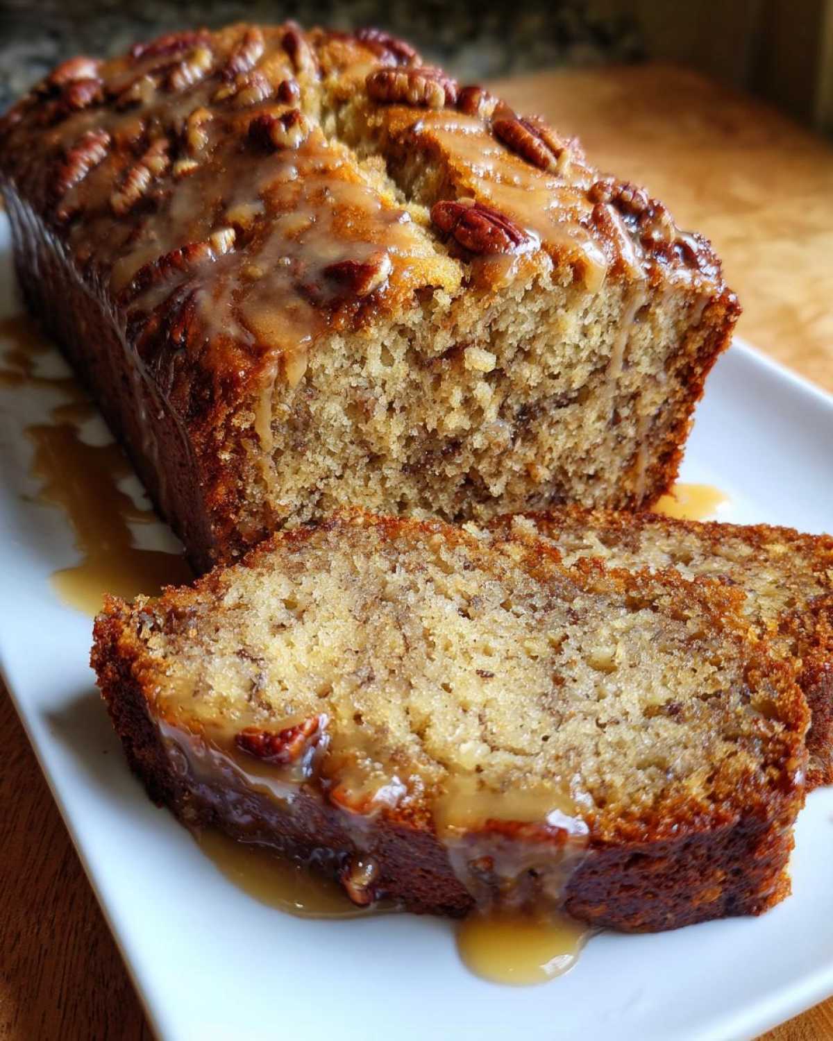 A loaf of sweet alabama pecan bread, partially sliced, drizzled with a thick caramel glaze and topped with pecans.