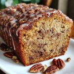 A close-up shot of a moist slice of sweet alabama pecan bread drizzled with white icing and garnished with whole pecans.