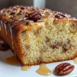 Close-up of a slice of moist sweet Alabama pecan bread drizzled with pecan glaze and served with whole pecans.