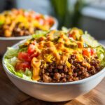 A close-up of a hearty cheeseburger bowl featuring seasoned ground beef, lettuce, tomatoes, pickles, and a generous drizzle of special sauce.