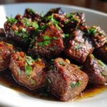 Close-up of tender, glazed crockpot steak bites swimming in rich sauce and topped with fresh chopped parsley.