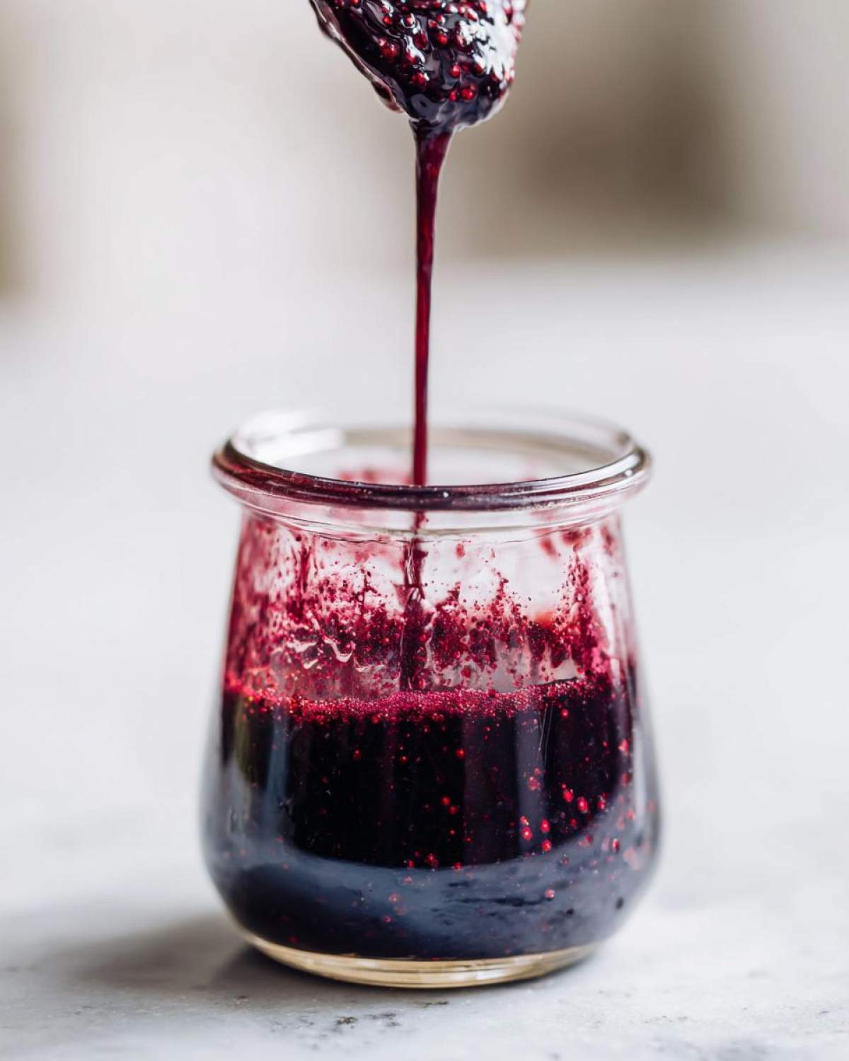 Close-up of thick, dark elderberry syrup recipe dripping from a spoon into a small glass jar.