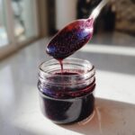 A spoonful of thick, dark purple elderberry syrup recipe dripping back into a small glass jar.