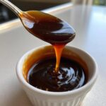 A spoonful of thick, glossy homemade teriyaki sauce dripping back into a small white bowl.