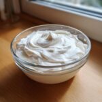 A clear glass bowl filled with thick, white, perfectly peaked royal icing recipe mixture.