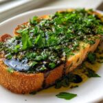 Close-up of toasted bread generously topped with a rich olive oil bread dip mixture and fresh parsley.