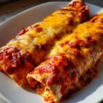 Two baked easy chicken enchiladas covered in melted orange and white cheese and red sauce on a white plate.