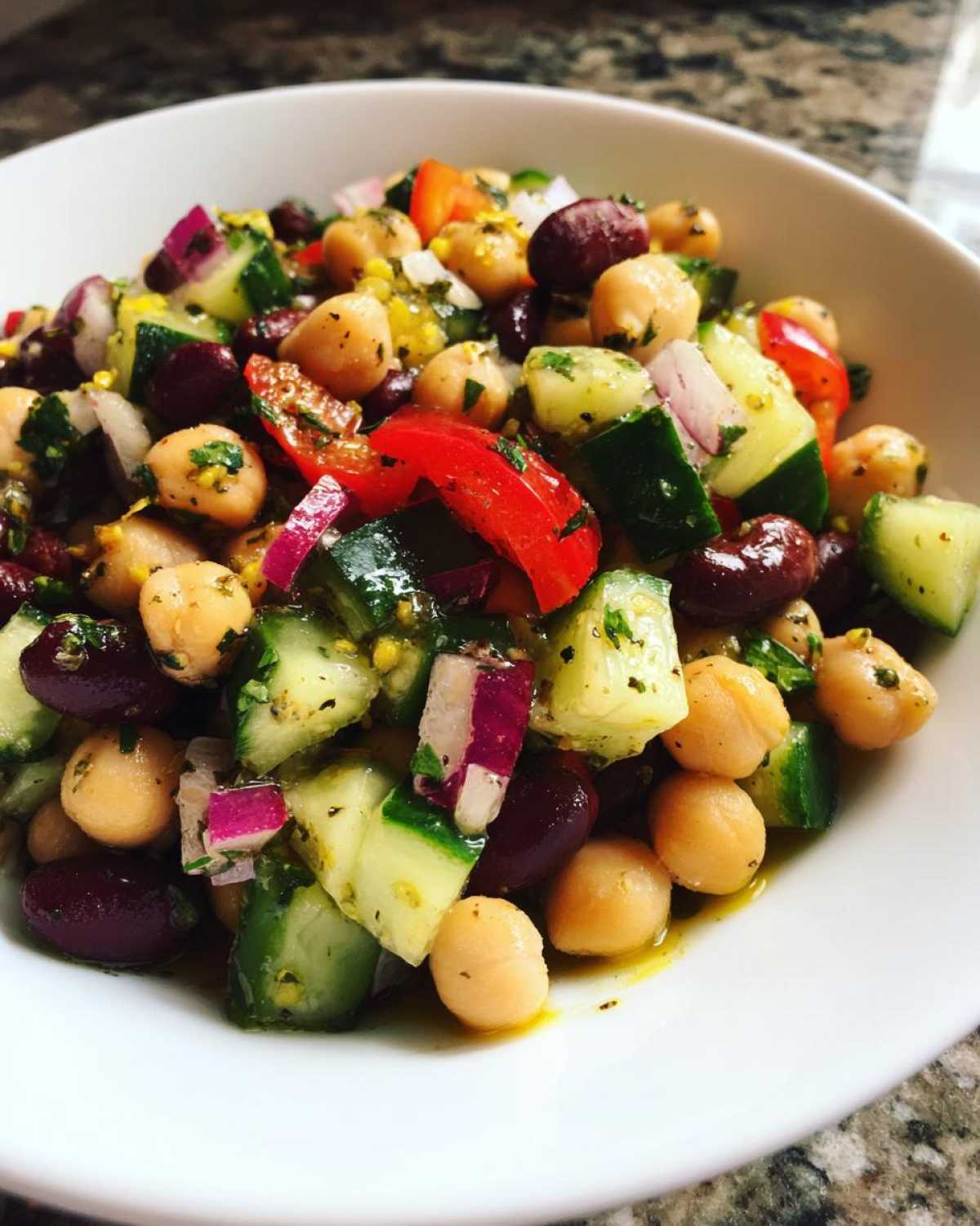 Close-up of a vibrant bean salad featuring chickpeas, kidney beans, cucumber, red onion, and red pepper in a light dressing.