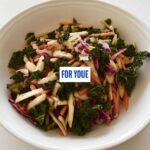 Close-up of a vibrant cabbage salad mix featuring shredded kale, red cabbage, white cabbage, and carrots in a white bowl.