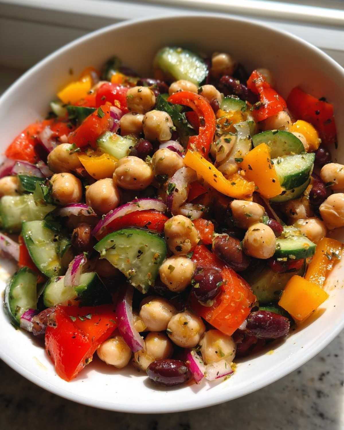 Close-up of a vibrant bean salad featuring chickpeas, kidney beans, cucumber, red onion, and bell peppers tossed in dressing.