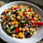 Close-up of a vibrant bean salad featuring chickpeas, cucumbers, red onion, bell peppers, and kidney beans.