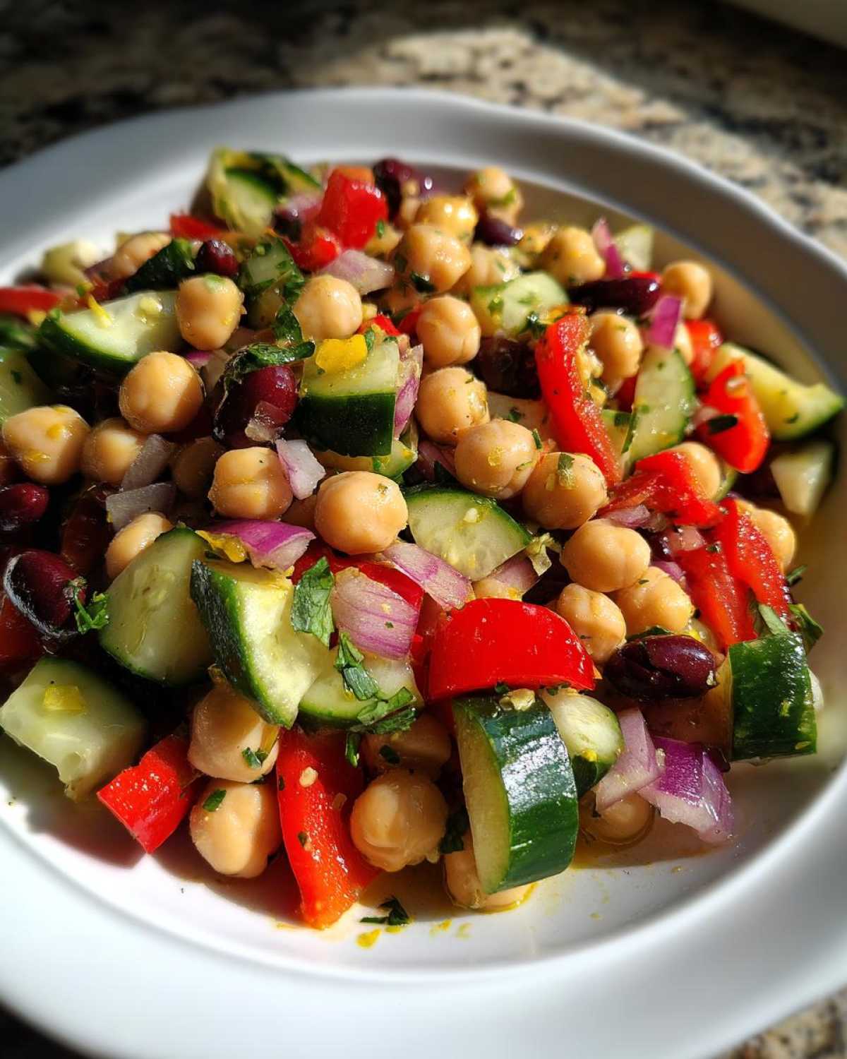 Close-up of a fresh, vibrant bean salad featuring chickpeas, cucumbers, red peppers, and red onion.