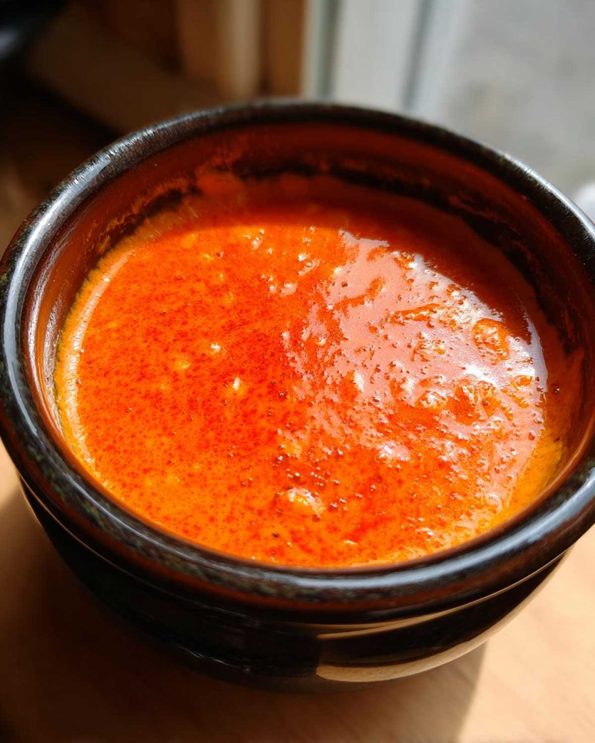Close-up of a bright orange, bubbling chili cheese dip served in a dark ceramic bowl.