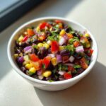 Close-up of vibrant Cowboy Caviar dip featuring black beans, corn, red onion, and tomatoes in a white bowl.